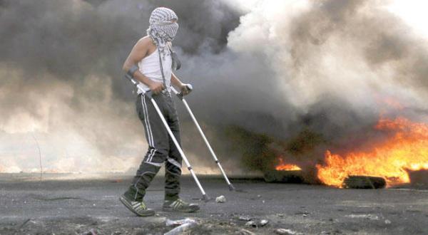 یک تظاهر کننده فلسطینی در حال راه رفتن با استفاده از عصا طی درگیری با سربازان اسرائیلی در نزدیکی رام الله – عکس از رویترز